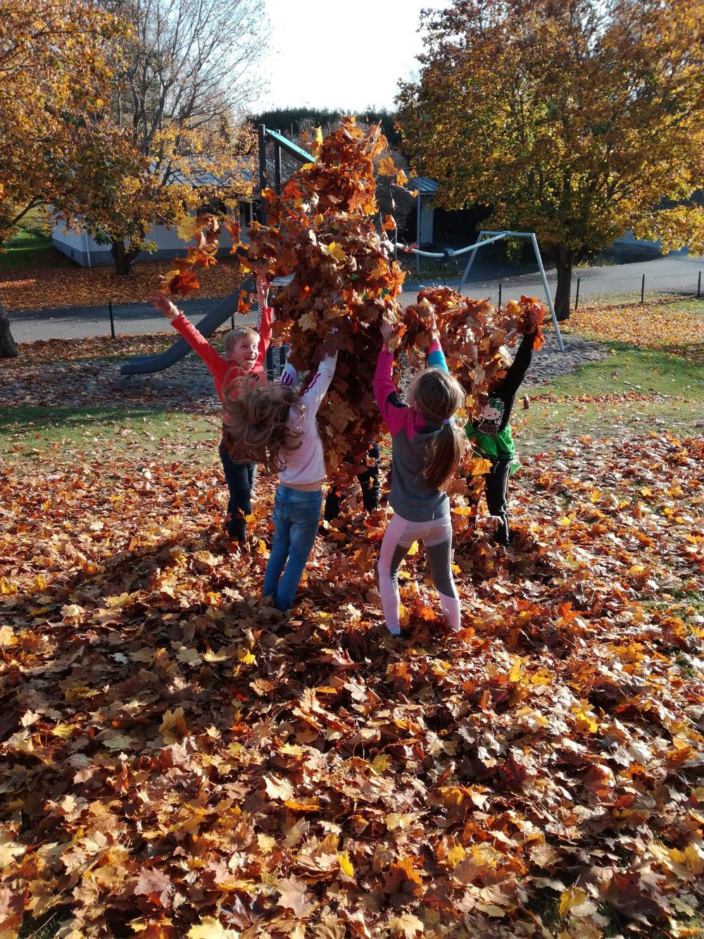 Glada barn som kastar upp höstlöv i luften.