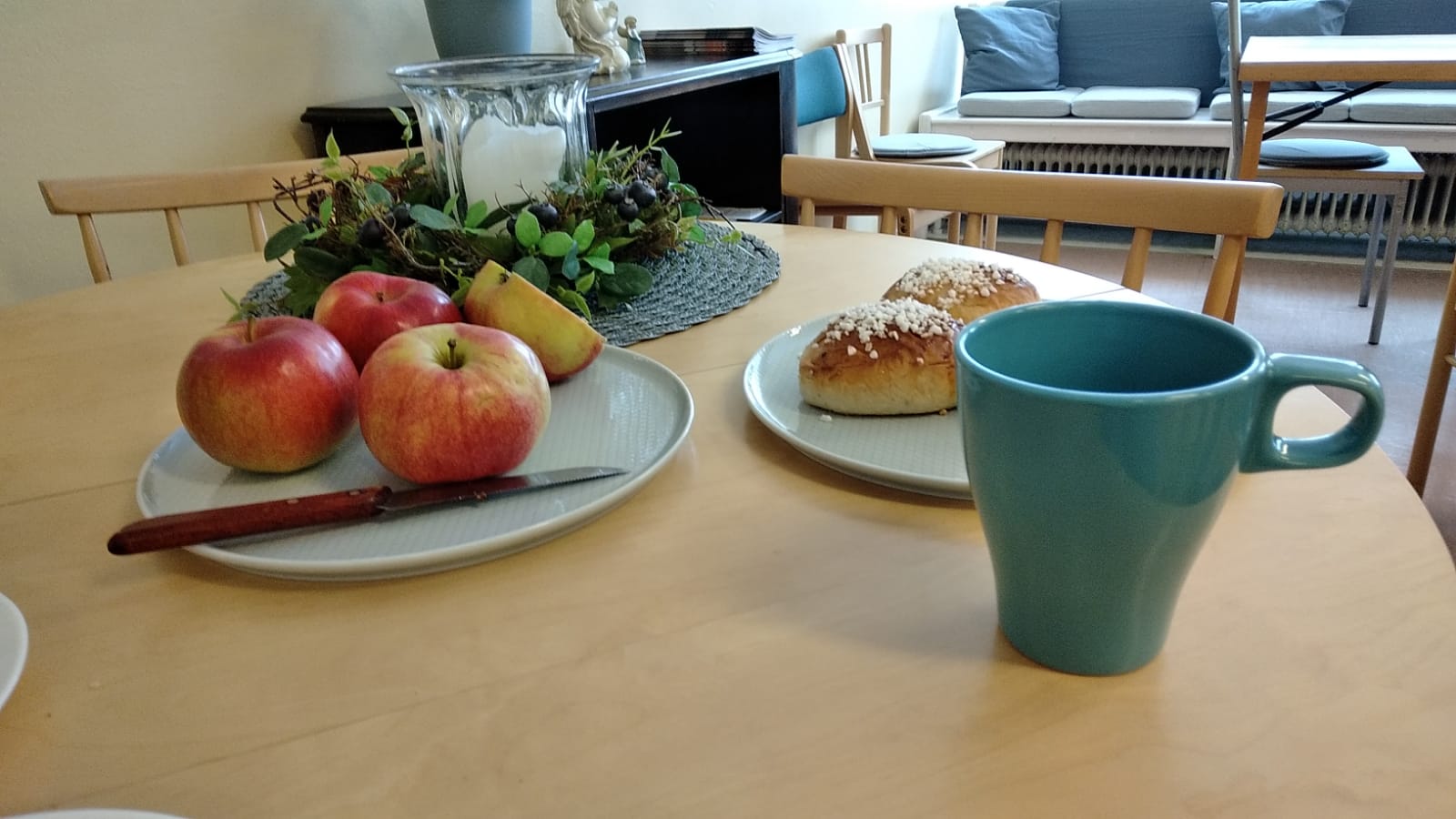 Gemenskapens vardagsrum En kaffekopp, bullar och frukt på ett bord.