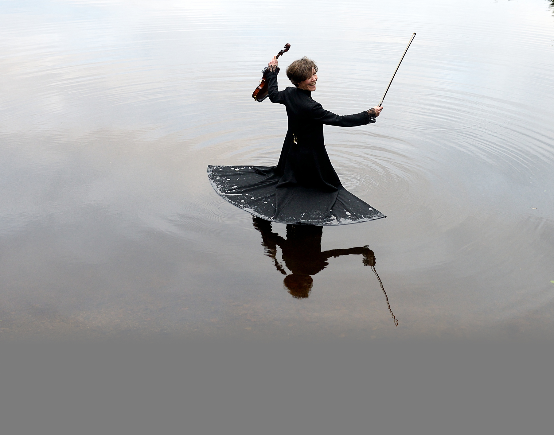 Bild av Johanna Almark med sin flytande svarta kappa och en violin i vänster hand och stråken i höger.